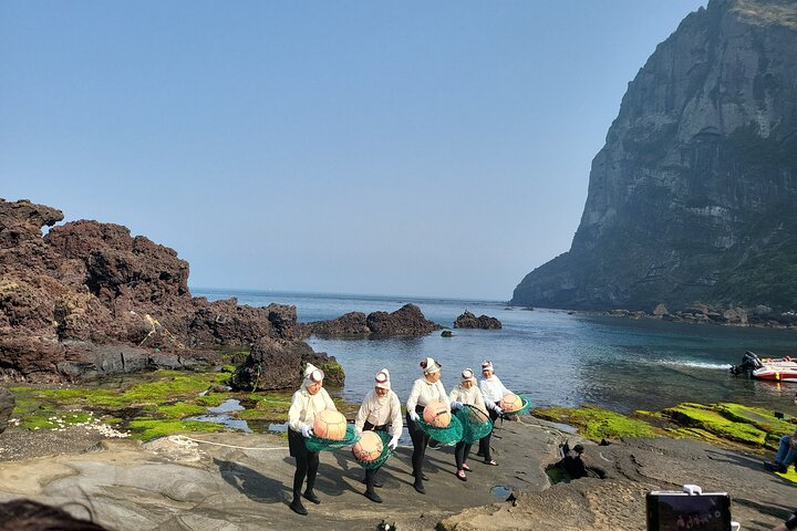 Experience the unique tradition of haenyeo divers as they collect seafood in the stunning surroundings of Jeju Island with breathtaking views of Seongsan Ilchulbong in the backdrop.